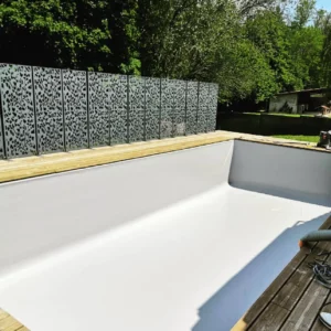 Chantier de piscine avec bassin blanc posé le long d'un mur en gabions, Vosges