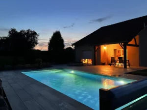 Piscine éclairée au crépuscule devant une maison avec terrasse en bois, Vosges