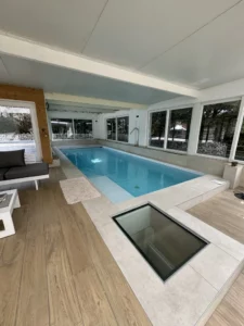 Piscine intérieure lumineuse bordée de baies vitrées et d'un sol bois, Vosges