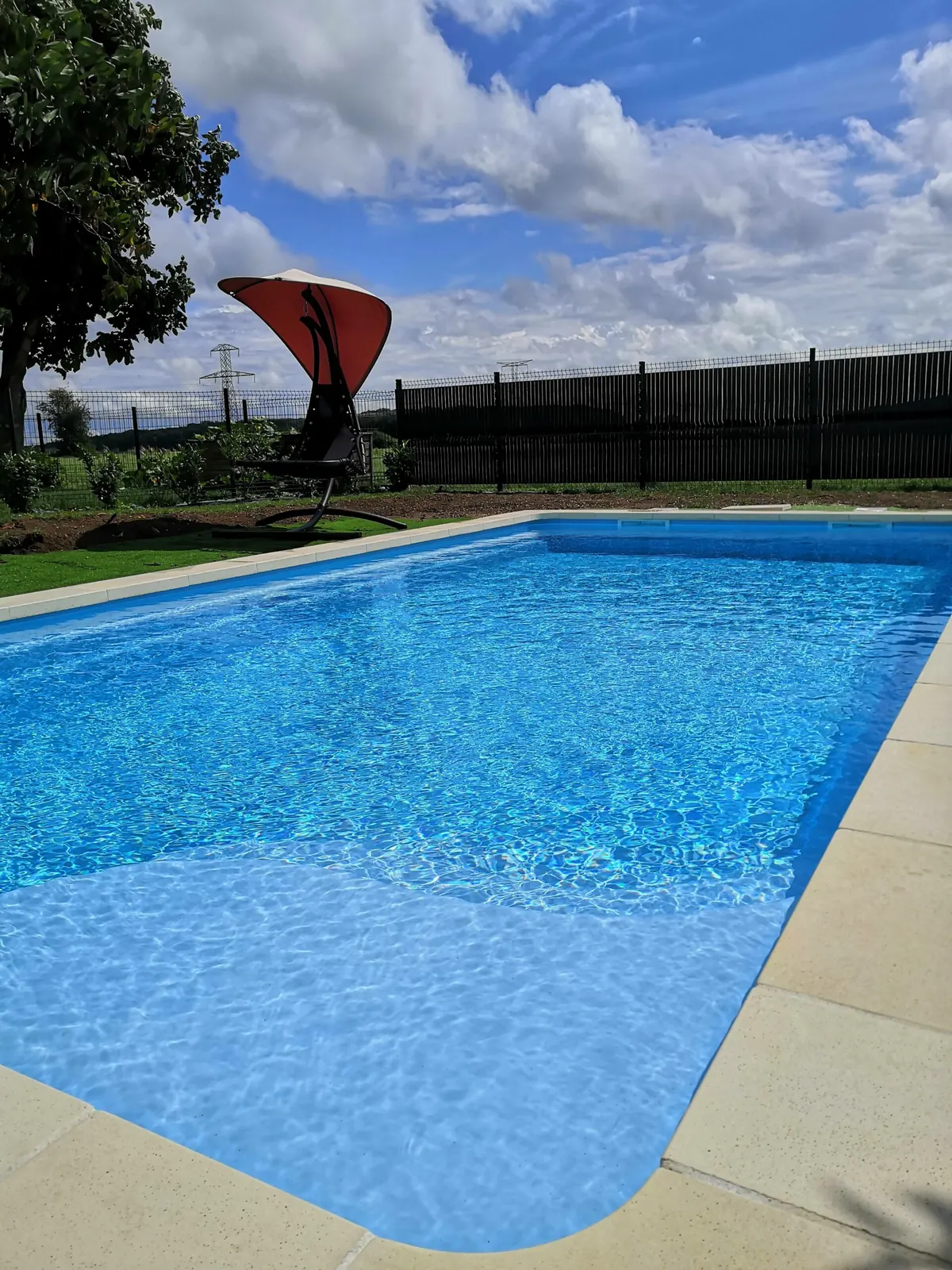 Piscine à angles arrondis avec liner bleu dans un jardin clos, Vosges