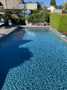 Piscine à l'eau bleue bordée d'une plage claire dans un jardin arboré, Vosges