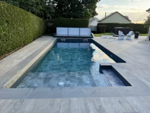 Piscine rectangulaire avec terrasse en pierre bordée d'une haie taillée, Vosges