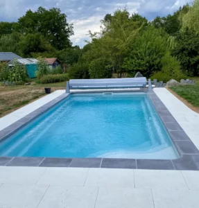 Piscine avec volet roulant hors-sol et margelles grises dans un jardin, Vosges