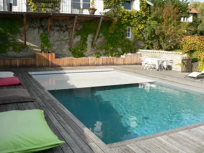 Piscine avec volet immergé bordée d'une terrasse en bois et de coussins de sol