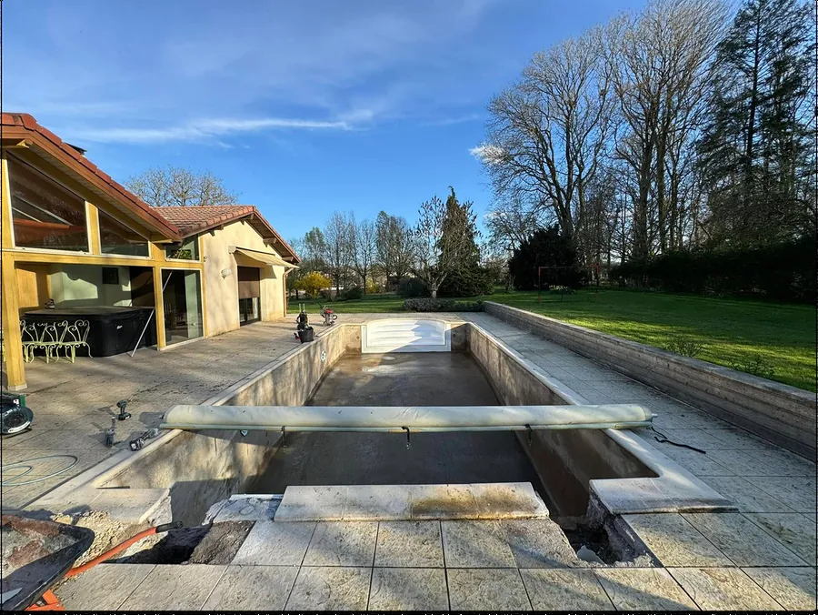 Piscine vide en béton brut avec margelles posées, maison contemporaine en arrière-plan