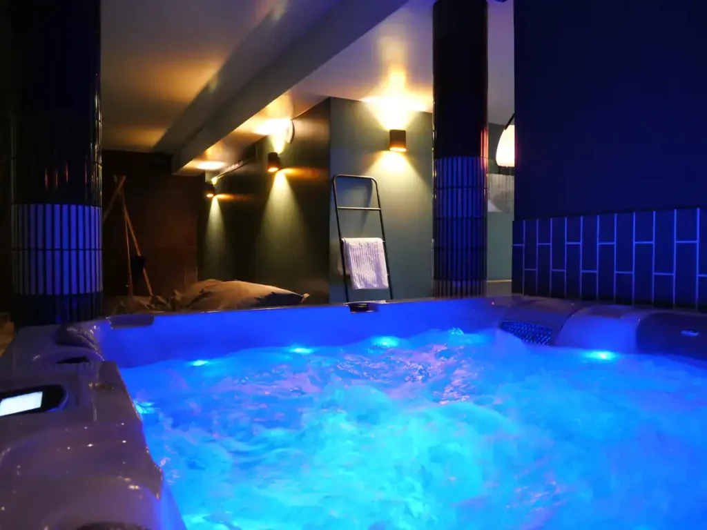 Spa intérieur éclairé en bleu dans une pièce sous charpente
