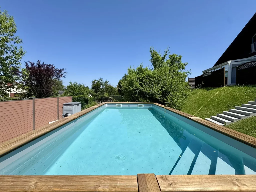 Piscine en bois hors-sol terminée, eau turquoise et margelles en bois, sous un ciel bleu à Golbey