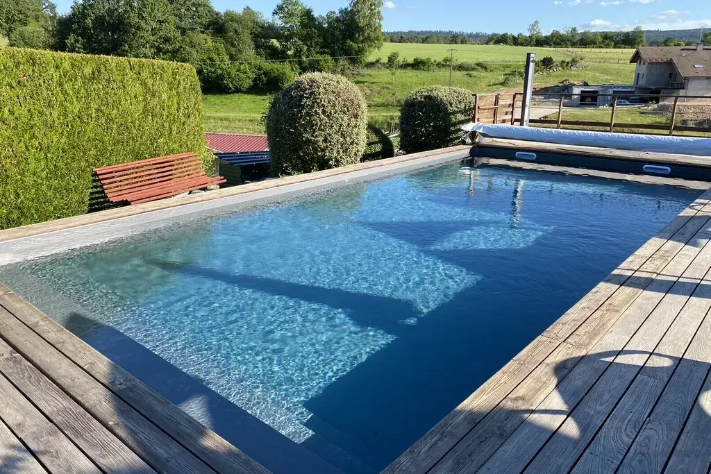 Eau cristalline d'une piscine à liner bordée d'une terrasse en bois, avec vue sur la campagne vosgienne